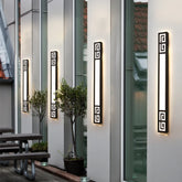 Four modern black geometric LED wall sconces mounted on a building exterior, illuminating a patio area.