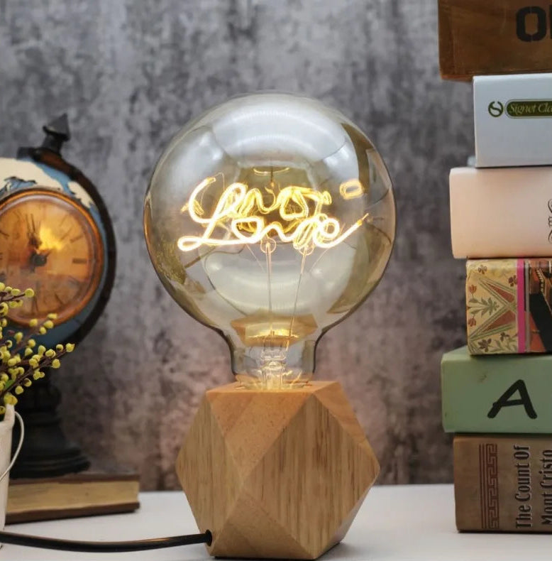Decorative light bulb with 'Love' text on a wooden base, surrounded by books and a clock.