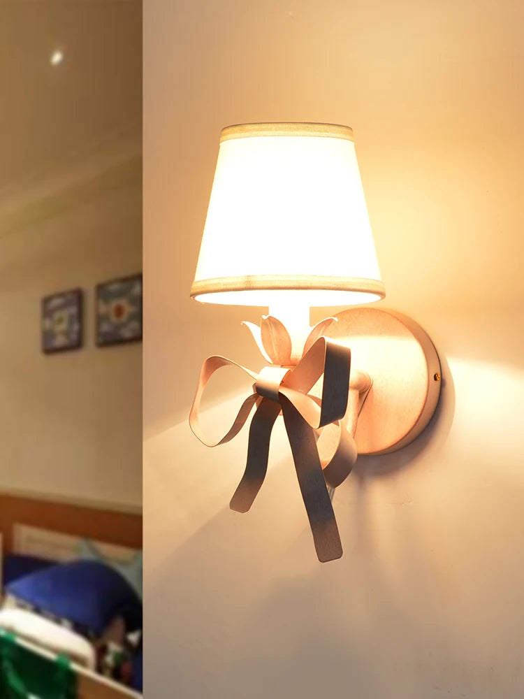 Single pink wall sconce with a fabric shade and a decorative ribbon bow, illuminated.