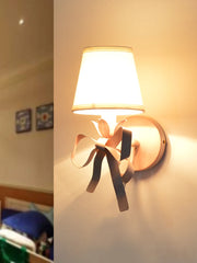 Single pink wall sconce with a fabric shade and a decorative ribbon bow, illuminated.