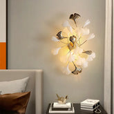 A modern gold wall sconce designed with multiple white ginkgo leaves, casting a warm glow on a neutral wall.
