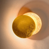 Gold layered circular wall sconce casting a warm glow on a textured wall.