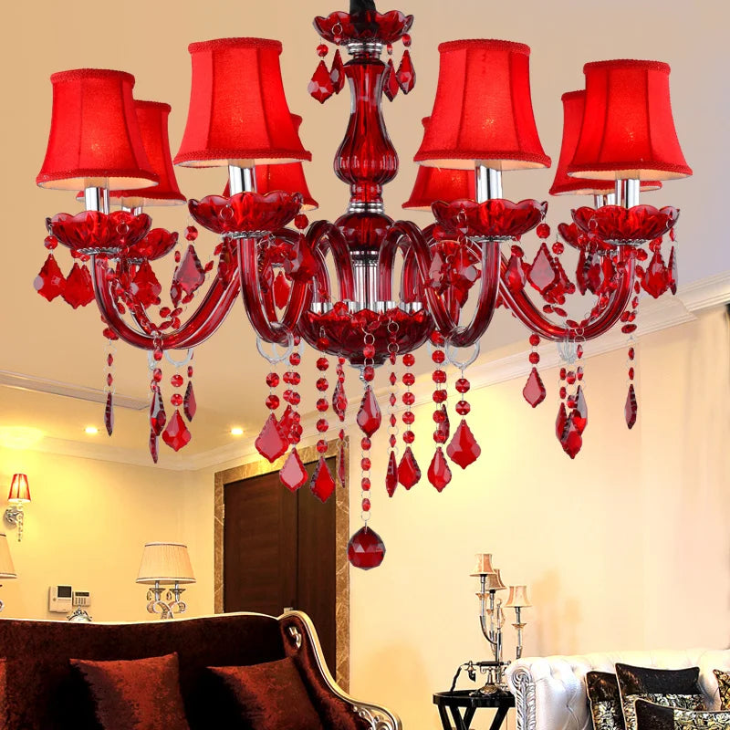 Red crystal chandelier with six fabric shades, suspended in a well-lit room with dark red furniture.