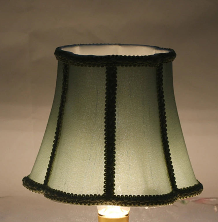 Sky blue fabric lampshade illuminated from within, showcasing its texture and dark trim against a dark background.