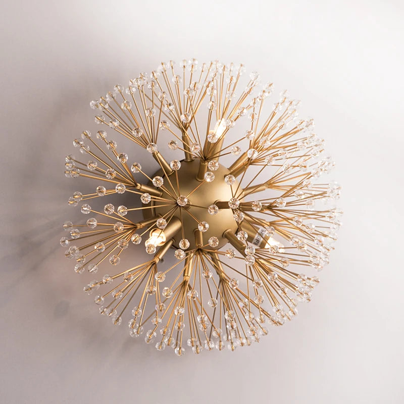 Close-up of a gold sputnik-style wall sconce with radiating arms covered in clear crystals against a white background.
