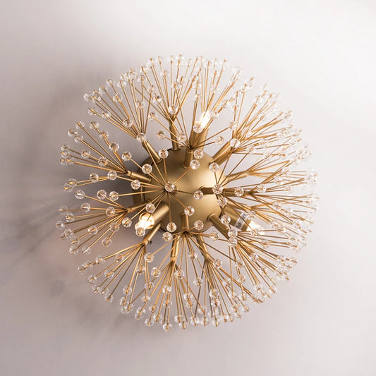Close-up of a gold sputnik-style wall sconce with radiating arms covered in clear crystals against a white background.