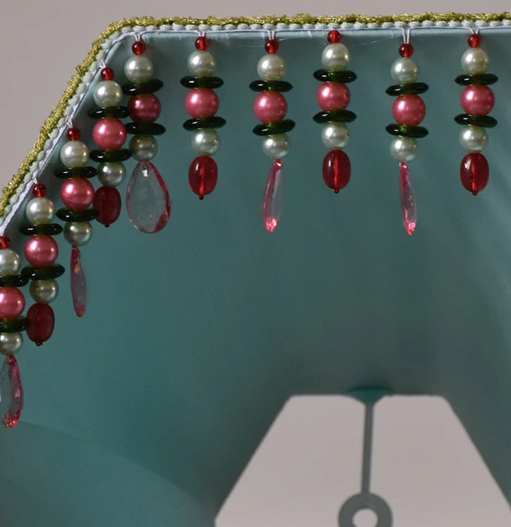 Detail view of the beaded tassels hanging from the bottom edge of a green pleated fabric lampshade.