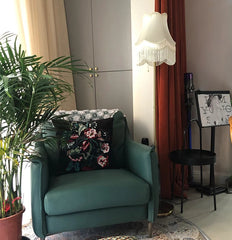 Floor lamp with a cream fabric bell lampshade with fringe in a living room setting