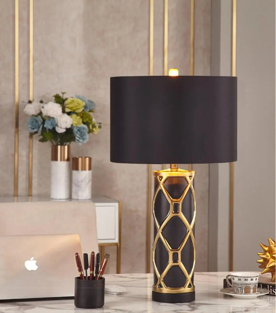 Decorative table lamp with black shade and gold base on a marble surface.