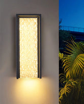 Wall-mounted outdoor light fixture on a gray wall with plants in the background