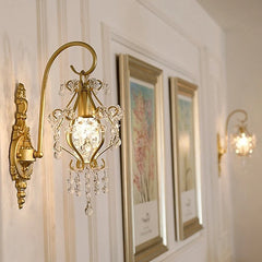 Two gold crystal wall sconces flank framed artwork on a white wall, demonstrating their decorative potential in a hallway or living space.