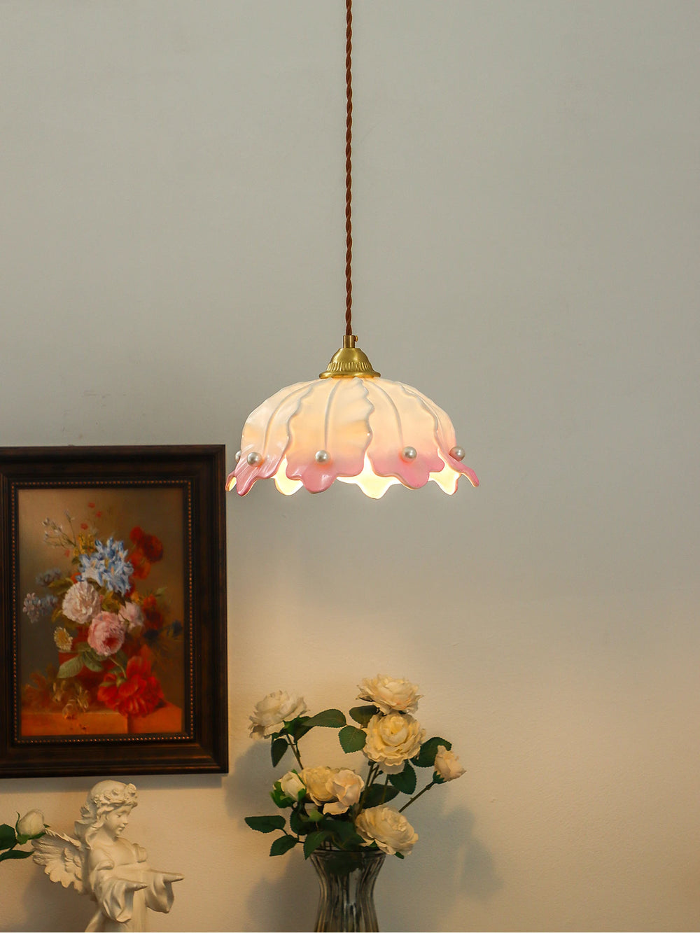 A pink and white ceramic petal pendant light with pearl accents, displayed in a room with a painting and flowers.
