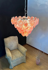 Pink glass chandelier hanging above a chair in a room with a white wall and wooden floor.