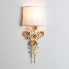 A gold floral crystal wall sconce with a white fabric shade against a white wall.