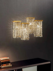 A wall-mounted gold crystal sconce with a rectangular top and cascading crystal strands, mounted on a dark wall.