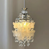 Close-up of a chrome pendant light with white butterfly-shaped shell accents and clear teardrop crystals.