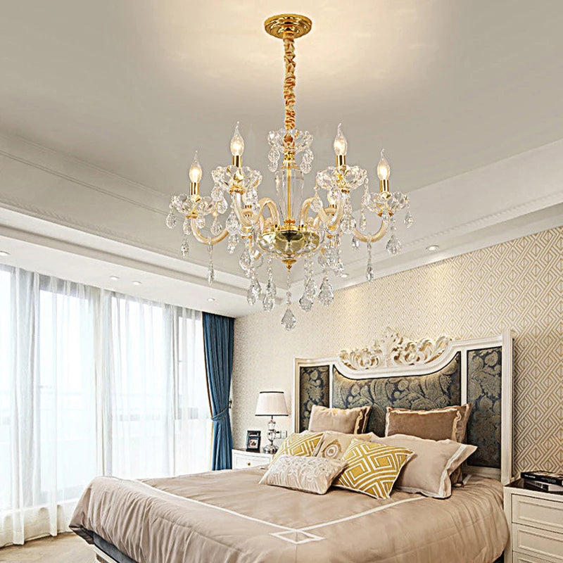 A gold crystal chandelier with multiple arms and dangling crystals, installed above a bed in a bedroom setting.