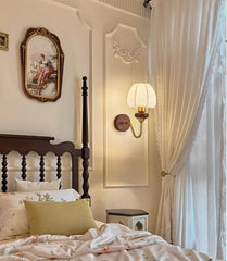 Bedroom with wooden bed, decorative pillows, wall sconce, and framed artwork.