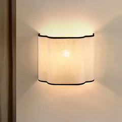 Wall-mounted light fixture with a textured white shade on a plain wall.