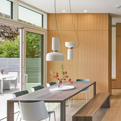 A dining room setting with two white pendant lights hanging above a wooden table, with natural light streaming in.