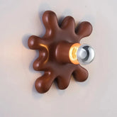 Pink starburst shaped ceramic wall sconce with a light bulb in the center, mounted on a white wall.