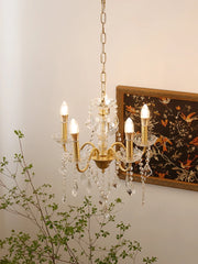Gold chandelier with crystal accents on a neutral wall with a decorative painting and plant.