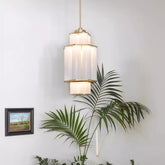 A gold and white acrylic tiered pendant light hanging in a room with a plant and a framed picture.