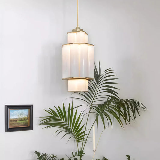 A gold and white acrylic tiered pendant light hanging in a room with a plant and a framed picture.