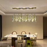 A modern dining room with a large, linear chandelier featuring multiple hanging gold and silver tubes with small light accents, suspended from a hexagonal ceiling plate.