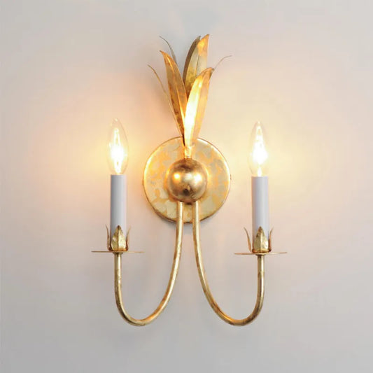Gold leaf wall sconce with two candle-style bulbs illuminating a white wall