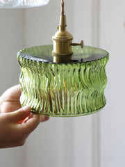 Green glass pendant light held by a hand against a neutral background