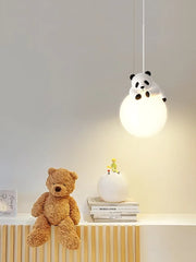 Panda-shaped pendant light hanging above a shelf with a teddy bear and books.