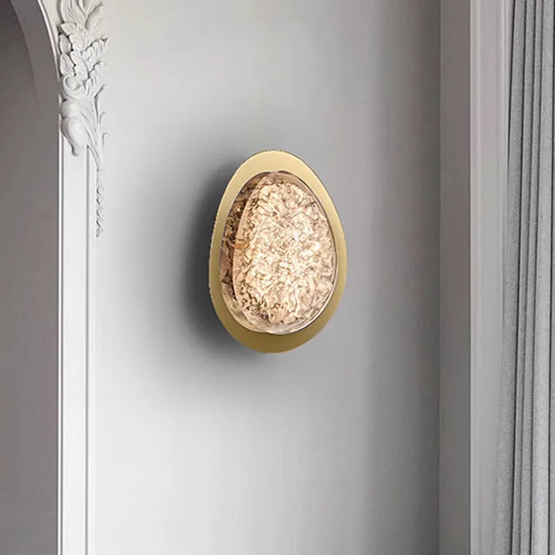 Gold textured resin egg-shaped wall sconce mounted on a white wall with ornate architectural molding.