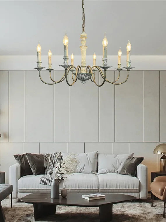 A white candelabra style chandelier installed in a modern living room above a sofa and coffee table.