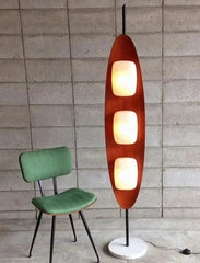Modern floor lamp with three light bulbs next to a green chair against a tiled wall.