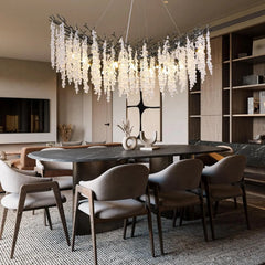 A curved, branch-like chandelier with hanging crystals, suspended above an oval dining table in a well-decorated room.