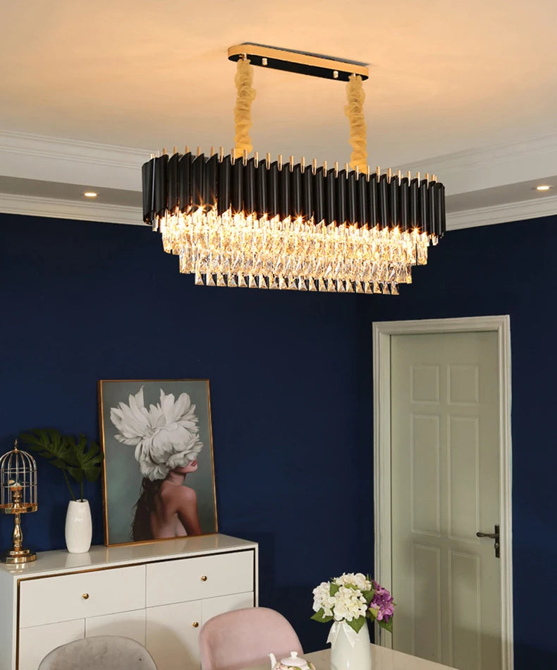 Modern chandelier hanging in a room with a blue wall, white dresser, and floral arrangement.