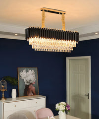 Modern chandelier hanging in a room with a blue wall, white dresser, and floral arrangement.