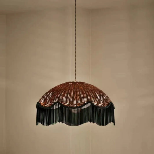 Woven rattan dome pendant light with a dark fringe hanging against a plain background