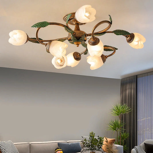 A gold multi-arm ceiling light with white tulip-shaped glass shades and green leaf accents, installed on a ceiling above a grey sofa.