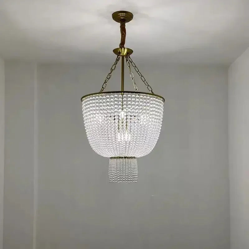 A clear crystal chandelier with a gold frame hangs from a ceiling in a softly lit room with white walls.