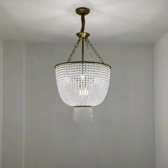 A clear crystal chandelier with a gold frame hangs from a ceiling in a softly lit room with white walls.