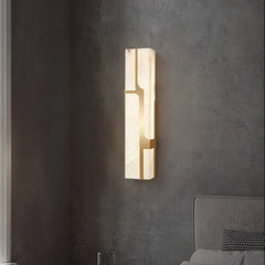 Modern wall sconce on a dark gray wall with a bed in the background