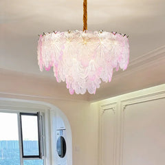 A pink-toned crystal leaf chandelier with a layered design, illuminated and hanging from a gold cord.