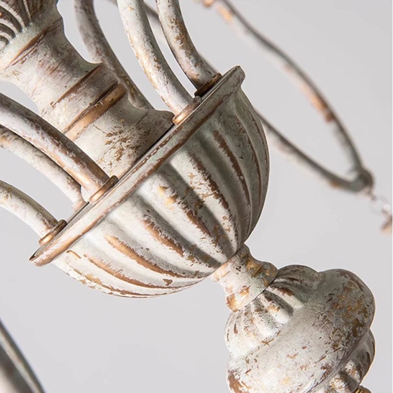 Detailed close-up of the central body of a distressed white iron chandelier, highlighting its ornate texture and finish.