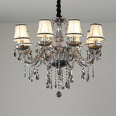 A close-up view of a smoke gray crystal chandelier with fabric shades and cascading crystal droplets against a white ceiling.