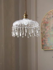 Crystal pendant light hanging against a neutral wall with a decorative mirror.