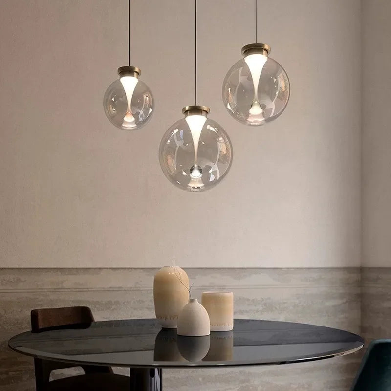 A cluster of clear glass globe pendant lights with metallic caps, arranged at different heights over a dark table.