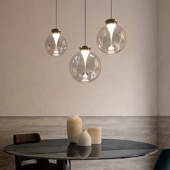 A cluster of clear glass globe pendant lights with metallic caps, arranged at different heights over a dark table.