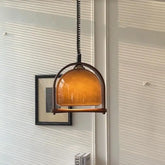 Amber glass dome pendant light with curved wood frame hanging indoors.